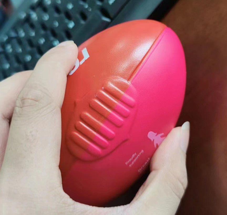 A vibrant red and pink custom aussie rules stress ball shaped like a football with textured grip ridges for workwear use