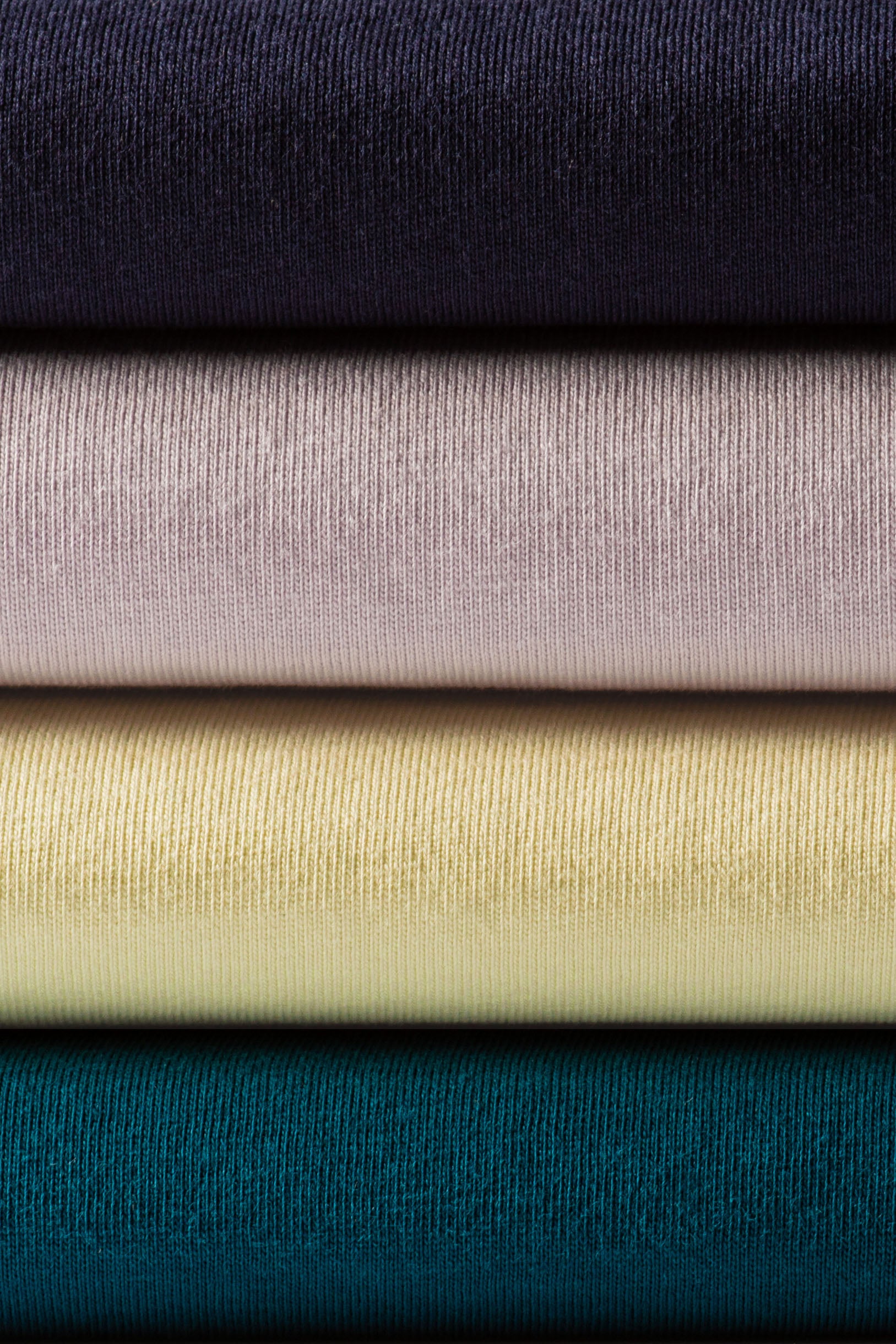 Stack of four neatly folded classic heavyweight ribbed knit t-shirts in navy mauve pale yellow and teal for workwear uniforms