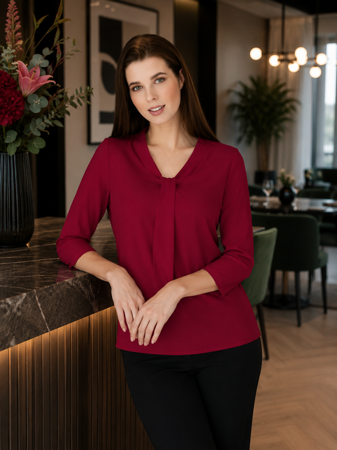 Woman in a red blouse standing in a modern indoor setting with decor elements.
