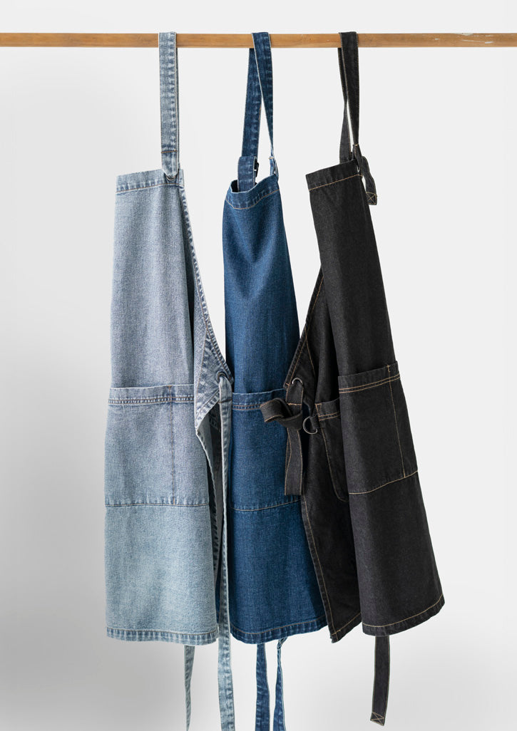 Three Clout Apron denim aprons in light blue, medium blue and black on wooden rod
