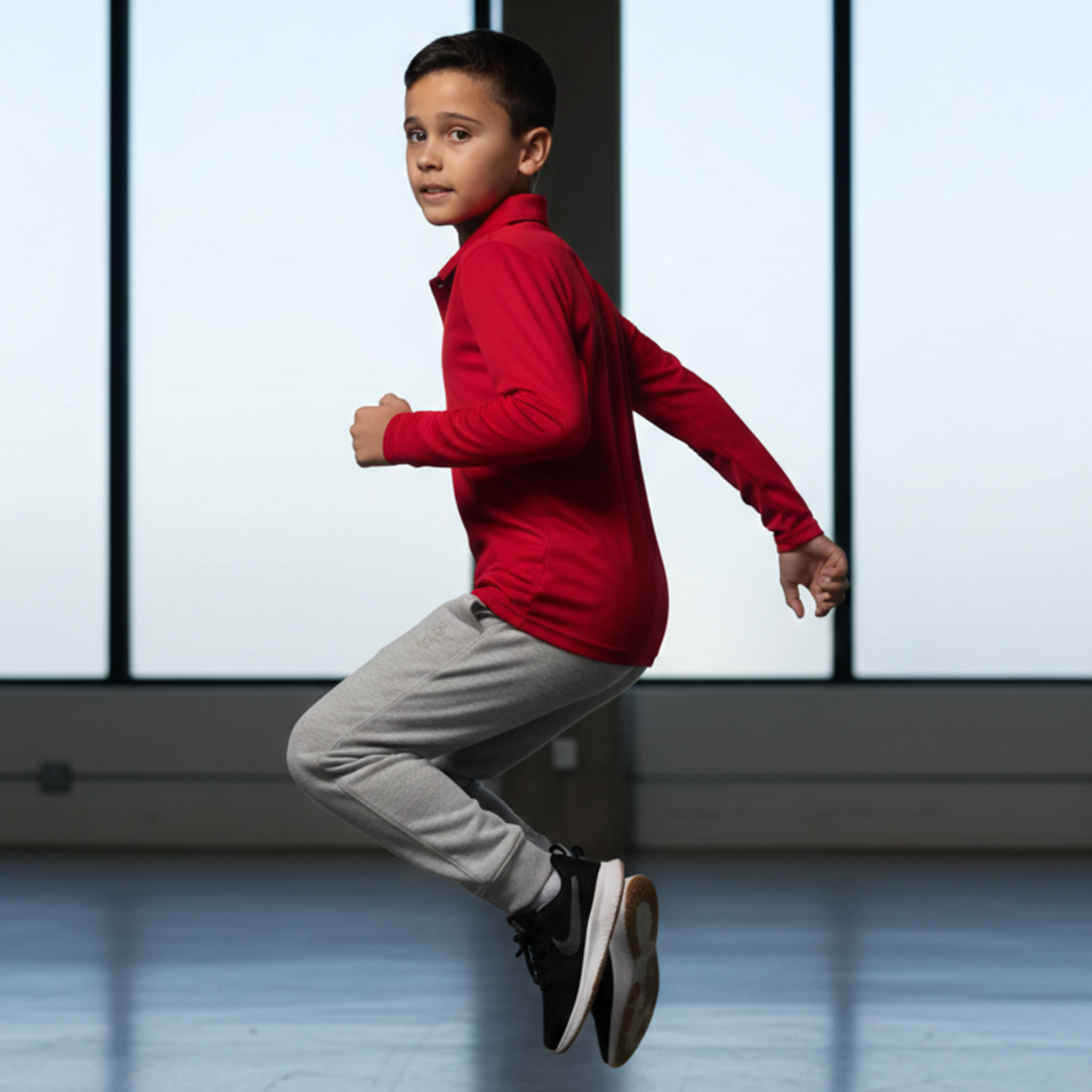 Young kid jumps in comfy Kids Botany LS Polo uniform, red shirt gray pants