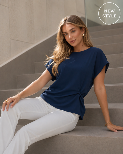 Woman wearing a navy blue top and white pants sitting on steps.