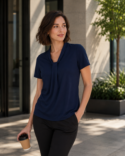 Woman in a navy blue top and black pants holding a coffee cup outdoors.