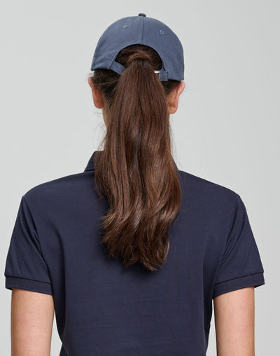 Person wearing a navy cap and dark blue shirt with long hair in a ponytail on a light gray background
