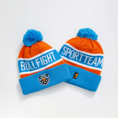 Orange and blue knitted pompom beanie with fluffy pom and white bullfight sportteam text perfect for workwear uniforms