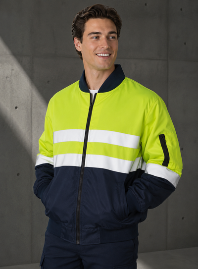 A man wearing a two-tone high-visibility jacket with a bright neon yellow-green upper section, white horizontal reflective stripes across the chest, and a navy blue lower section and collar, standing against a gray concrete wall.
