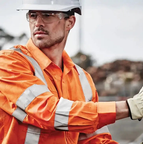 Construction worker wearing orange hi vis safety suit with reflective stripes and white hard hat in outdoor Australian worksite