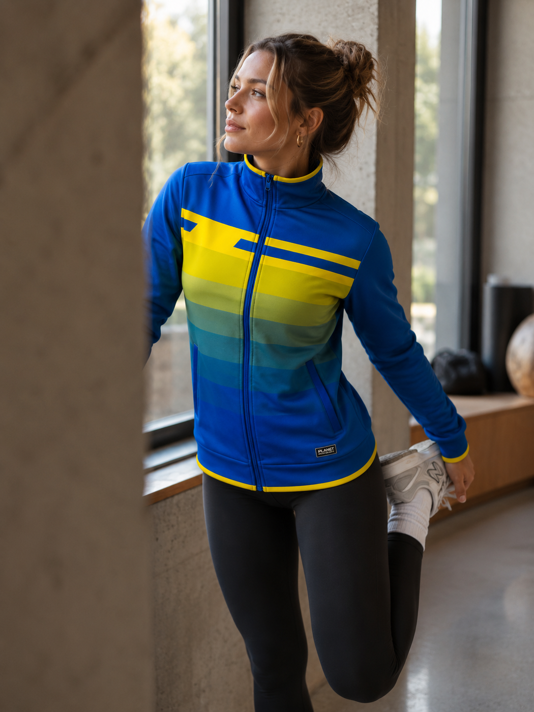Woman in a blue and yellow jacket stretching indoors