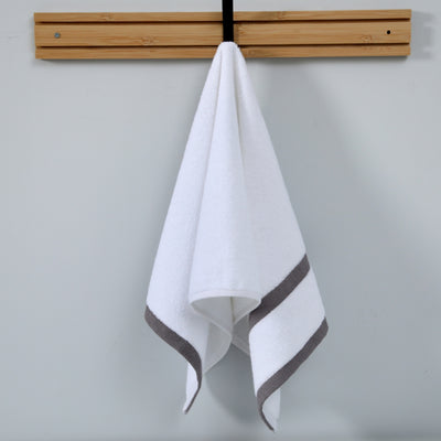 White towel with gray border hanging on a wooden rack against a light gray background