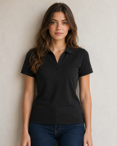 A woman wearing a black short-sleeve polo shirt and dark blue jeans, standing against a neutral light gray wall.