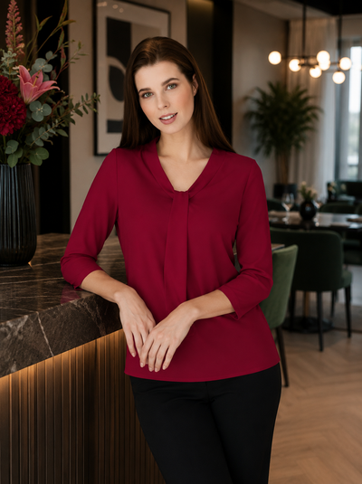 Woman in a red blouse standing in a modern indoor setting with decor elements.
