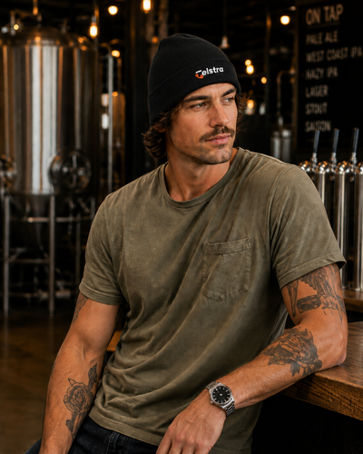 A man in a brewery setting wearing a black beanie with a white and red 'Palabra' logo and an olive green t-shirt.