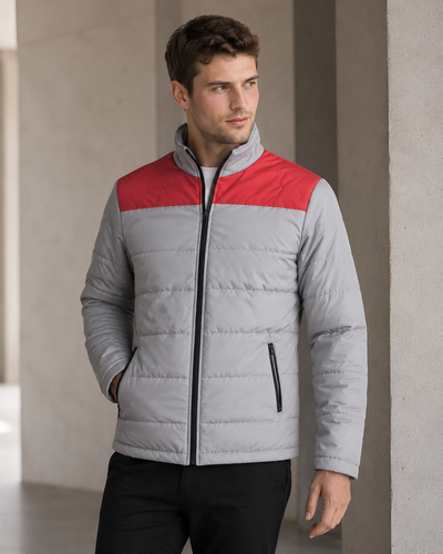 A man wearing a light gray puffer jacket with a contrasting red yoke across the chest, standing in a modern concrete corridor.