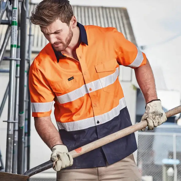 Man wearing high visibility orange work shirt in Australia holding tool on outdoor construction site for safety workwear
