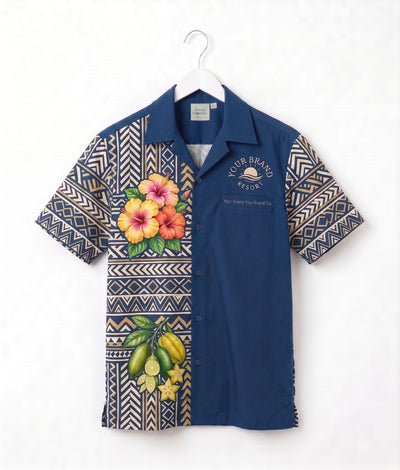 A short-sleeve button-up camp shirt hanging on a white hanger against a white wall. The shirt features a navy blue body with geometric patterned sleeves and lower front panel, decorated with tropical floral and fruit prints including hibiscus flowers and bananas.