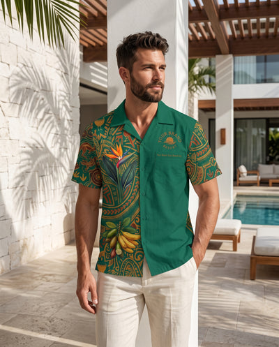 A man wearing a green short-sleeve button-up shirt with a tropical paisley print and a small embroidered logo on the chest, standing in a modern outdoor patio setting next to a swimming pool.