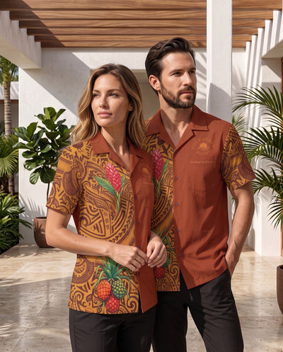 A man and a woman wearing matching tropical resort shirts in a sunlit outdoor patio setting. The woman's shirt is brown with colorful pineapple and floral prints, and the man's shirt is a solid rust-brown color with a subtle logo on the chest.