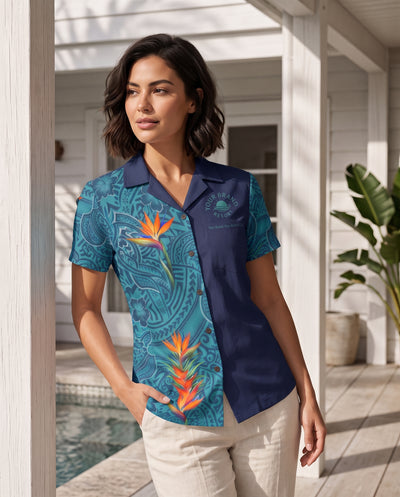 A woman stands on a porch wearing a short-sleeve collared button-up shirt with a split design: one side is teal with tropical floral and paisley print, and the other side is solid navy. The shirt has a small embroidered logo on the chest.