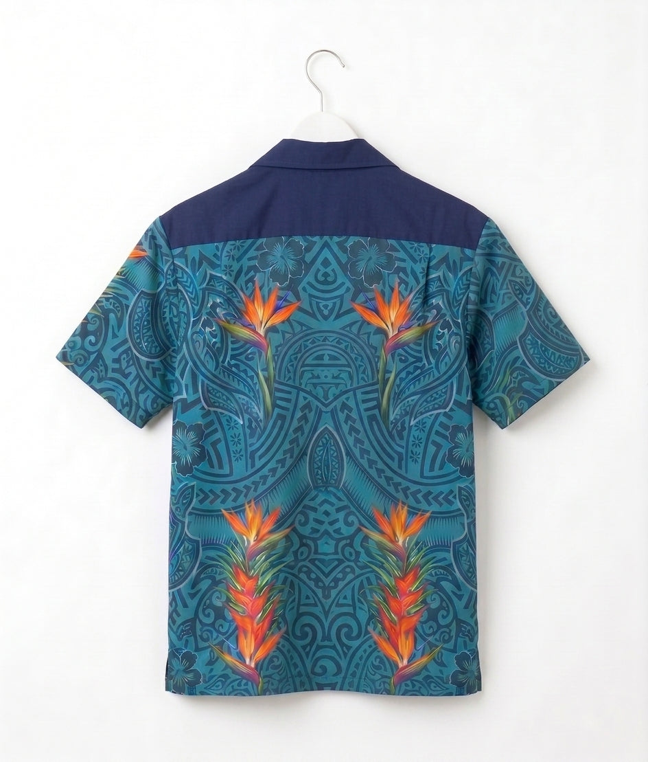 A short-sleeve camp collar shirt shown from the back, hanging on a white hanger against a plain white wall. The shirt features a dark navy blue upper yoke and a lower body with a teal and blue paisley pattern overlaid with three large orange and yellow tropical bird-of-paradise flowers.