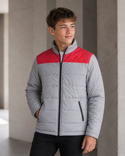 A young man wearing a light gray puffer jacket with a contrasting red yoke and black zipper details, standing in a modern concrete corridor.