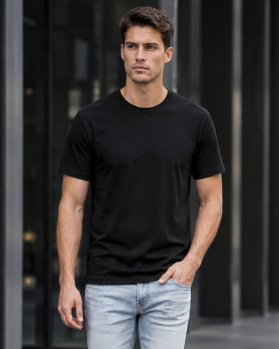 Man wearing a black t-shirt and light blue jeans against a dark background