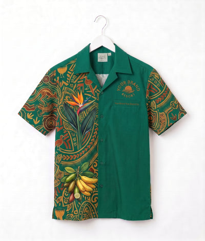 A green short-sleeve button-up shirt with a tropical and Polynesian-inspired print on the sleeves and left side, hanging on a white hanger against a white background. The right side is solid green with 'YOUR BRAND WEAR' printed on the chest.