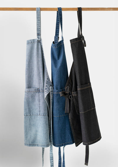 Three Clout Apron denim aprons in light blue, medium blue and black on wooden rod
