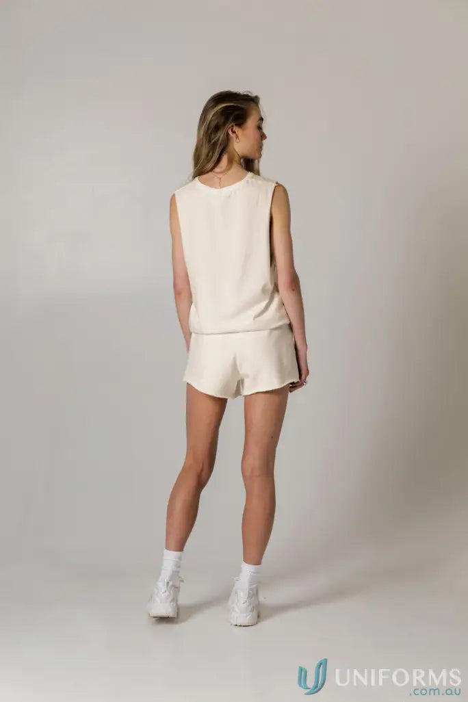 Woman in cream cotton tank top with raw cut sleeve and nameless chest embroidery