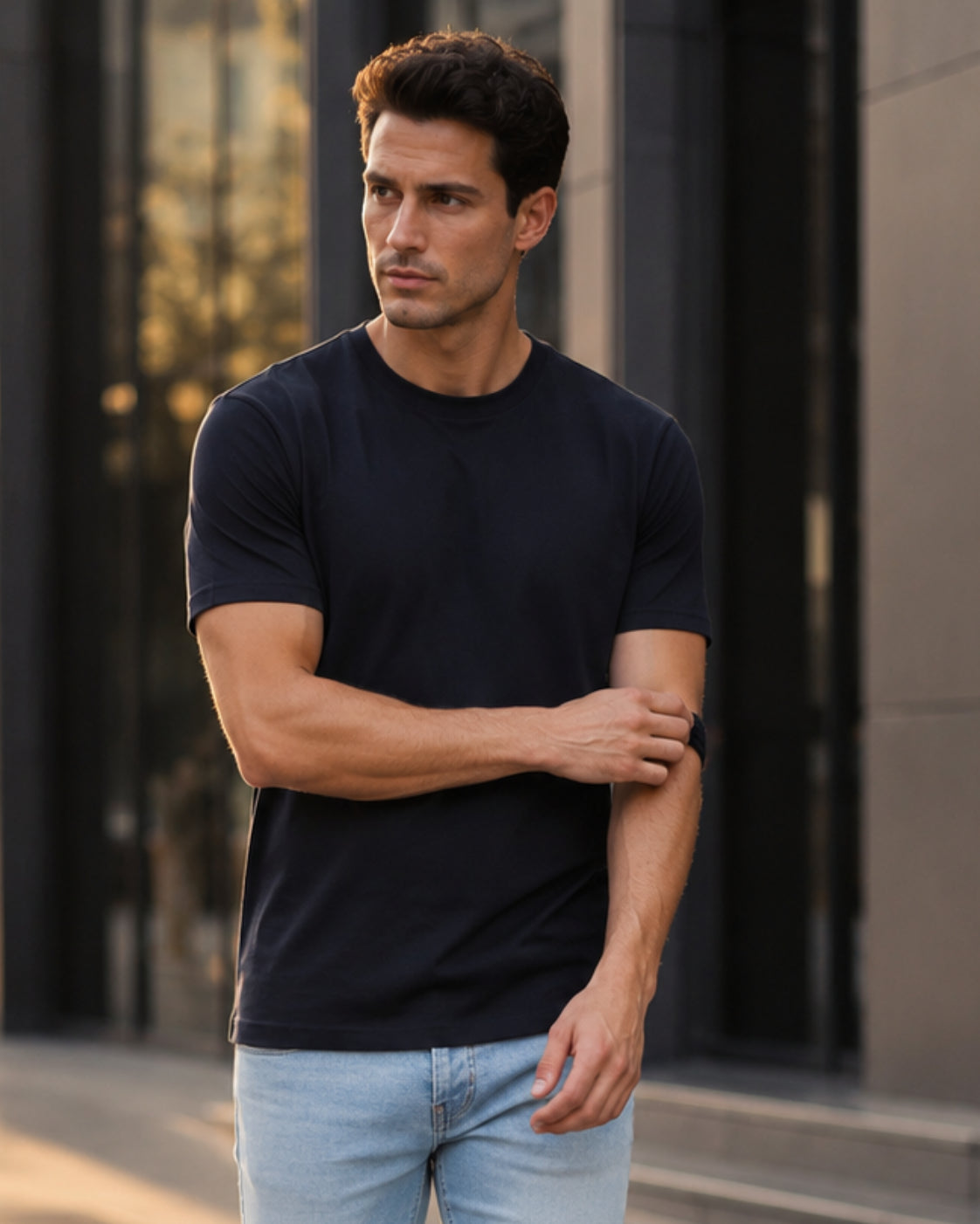 Man wearing a black t-shirt and light blue jeans standing outdoors.