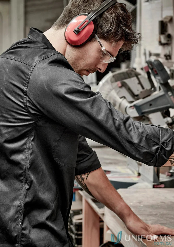 A man in a workshop wears red over-ear headphones and a 1Komma5 light weight tradie shirt perfect for workwear uniforms