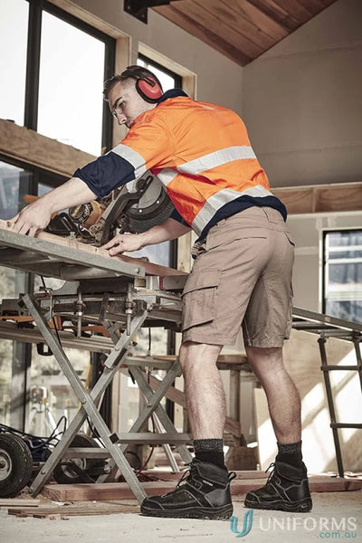 Construction worker using a chop saw wearing SYZMIK Streetworx Curved Cargo Shorts for men