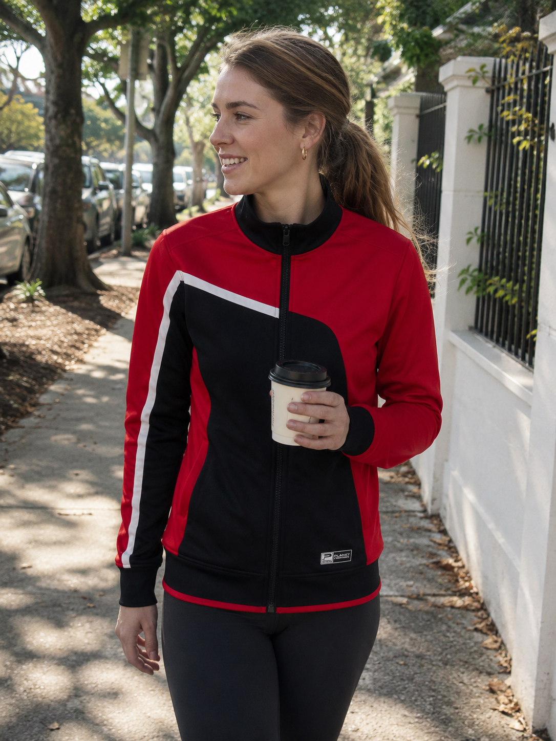 Woman in a red and black jacket holding a coffee cup on a sidewalk.